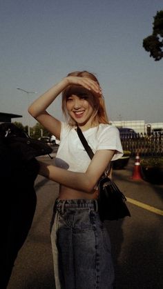 a woman standing on the side of a road holding her hair in front of her head