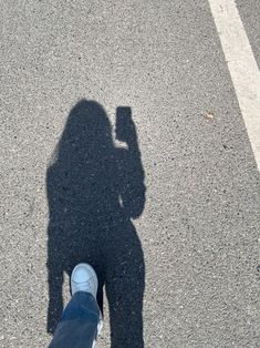 the shadow of a person's feet and their phone on the ground in an empty parking lot