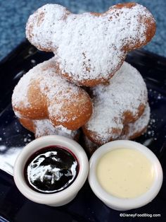 powdered sugar coated doughnuts and dipping sauce on a black plate with blue background