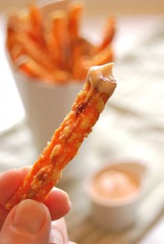 a hand holding up a piece of food with sauce on it and french fries in the background