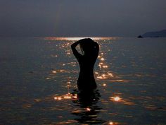 a woman standing in the water with her back turned to the camera and sun reflecting on the water
