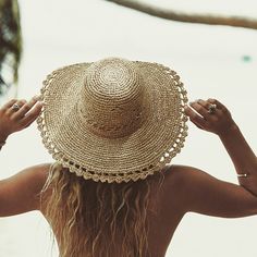 a woman with long hair wearing a straw hat on her head looking out at the ocean