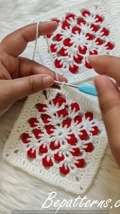 someone is crocheting a square with red flowers on it, while another person holds the yarn