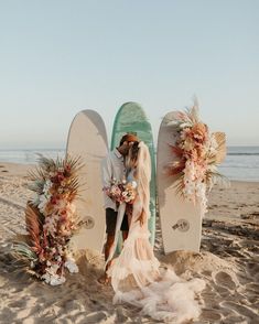 a bride and groom kissing on the beach next to surfboards decorated with floral arrangements