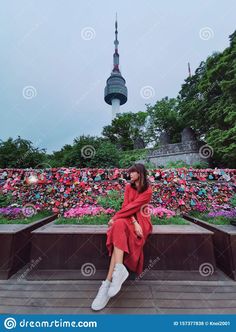 a woman in red dress sitting on steps near flowers and a building with a spire