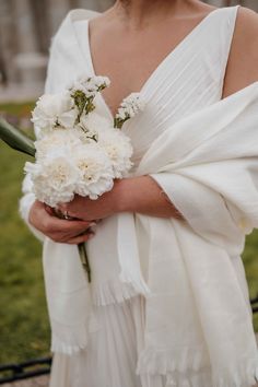 a woman wearing a white dress holding a bouquet of flowers in her hand and wrapped in a shawl