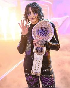 a female wrestler is holding up her wwe belt and giving the peace sign with both hands