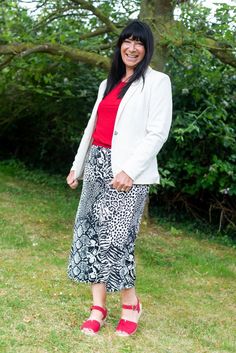 a woman standing in front of a tree wearing a white blazer and red top