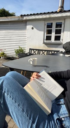 a person sitting at a table with a book in their lap and holding a coffee cup