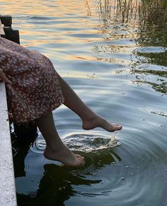 a woman sitting on the edge of a dock next to water with her feet in the water