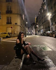 a woman sitting on a bench in the middle of an empty city street at night