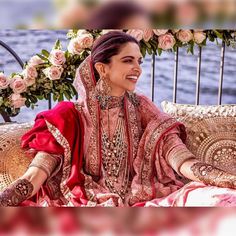 a woman sitting on top of a couch wearing a red and gold wedding dress with flowers in the background