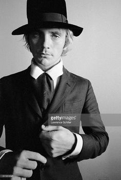 a young man in a suit and hat poses for a black and white photo with his hands on his hips