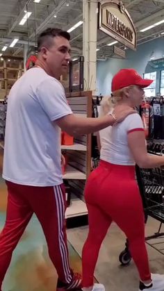 a man and woman in red pants are walking through a store aisle with shopping carts