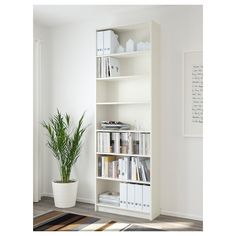 a white book shelf filled with books next to a potted plant