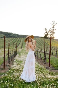 a woman in a white dress and straw hat standing in the middle of a vineyard