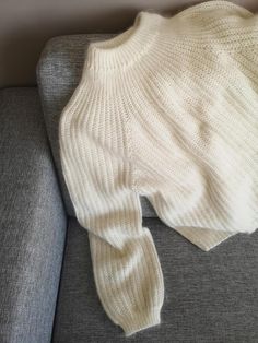 a white sweater laying on top of a gray couch