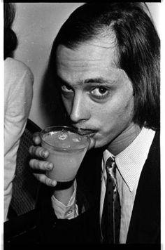 black and white photograph of a man drinking from a glass with liquid in it while looking at the camera