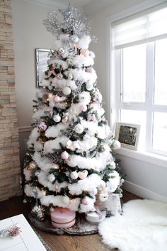 a white christmas tree with pink and silver ornaments on it in front of a window