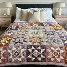 a bed with a purple and orange quilt on it's headboard next to two nightstands