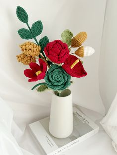 a crocheted flower arrangement in a white vase on top of a stack of books