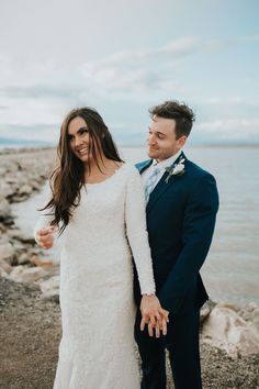 a bride and groom standing next to each other near the water on their wedding day