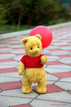 a teddy bear holding a heart shaped balloon on the ground with it's mouth open