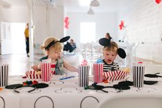 two children sitting at a table with mickey mouse ears on their heads and popcorn boxes in front of them