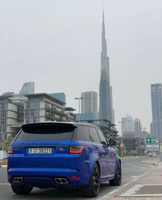 a blue range rover parked in front of a large city