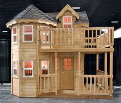 a wooden dollhouse with stairs and windows on the front porch, in an indoor setting