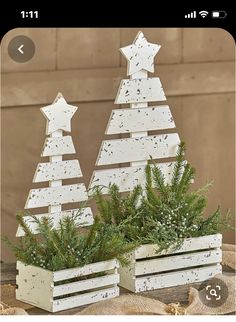 two white wooden christmas trees sitting on top of a table next to each other with pine branches in them