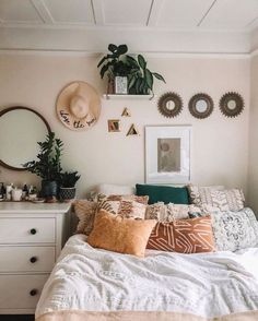 a bedroom with white walls and lots of pillows on the bed, plants hanging above