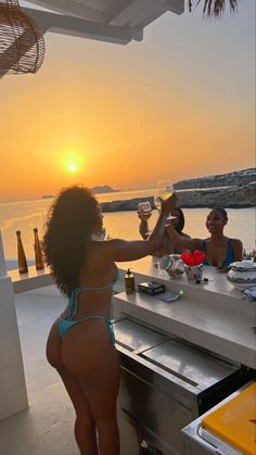 two women in bikinis toasting with wine glasses on a bar overlooking the ocean