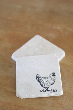 two napkins with a chicken drawn on them sitting on a table next to each other