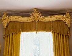an ornate gold curtain hanging in front of a window with yellow drapes and curtains