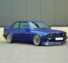 a blue bmw is parked in front of a building with its hood up and the door open