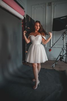 a woman in a short white dress posing for a photo with her hands on her hips