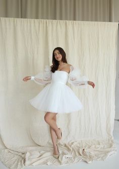 a woman in a white dress is posing for a photo with her arms spread out