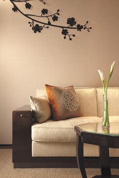 a white couch sitting next to a table with pillows on it and a vase filled with flowers