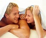 a man and woman laying in bed under a blanket smiling at each other with their eyes closed