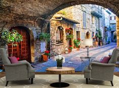 a living room with two chairs and a table in front of an archway that has potted plants on it