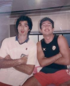 two men sitting next to each other with their arms crossed in front of the camera