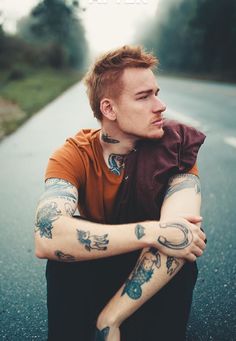 a man sitting on the road with his arms crossed and tattoos on his arm,