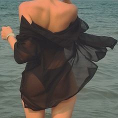 a woman standing in the water with her back to the camera, wearing a black dress