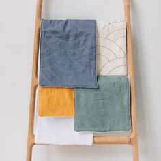 four different colored towels folded on top of a wooden chair next to a white wall