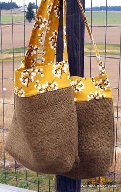 two bags hanging from a fence with flowers on the front and back straps, both in burlap