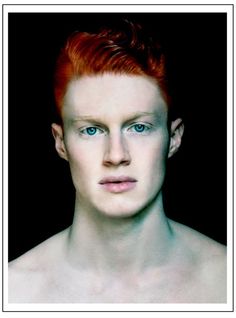 a man with red hair and blue eyes looks at the camera while wearing no shirt