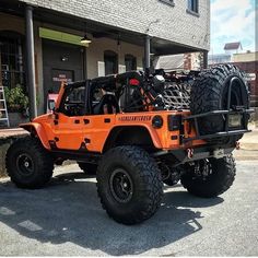 an orange jeep parked in front of a building with four tires on it's flatbed