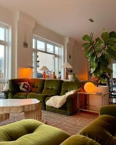 a living room filled with lots of green furniture and large plants in the window sill