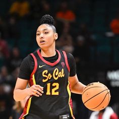 a female basketball player holding a ball in her hand and wearing a black jersey with the number 12 on it